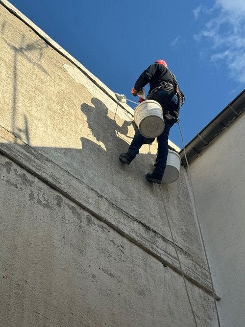 Operario descolgado con cuerdas y cubos trabajando en una fachada